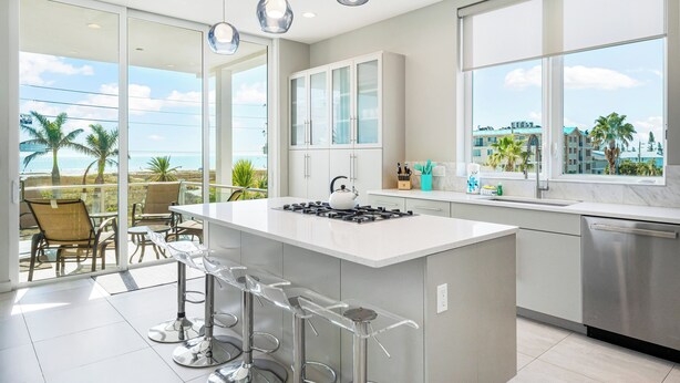 Eine moderne Küche mit einer großen Kochinsel, Barhocker und Blick aufs Meer.