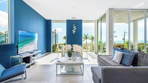 Ein modernes Wohnzimmer mit großem Fernseher, einer Couch, einem Couchtisch und einem Balkon mit Meerblick.