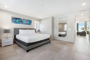 Um quarto moderno com uma cama grande, mesas de cabeceira, um espelho e um quadro abstrato colorido na parede.