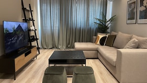 Een moderne woonkamer met een flatscreen televisie, een modulaire bank, een salontafel en een plant.