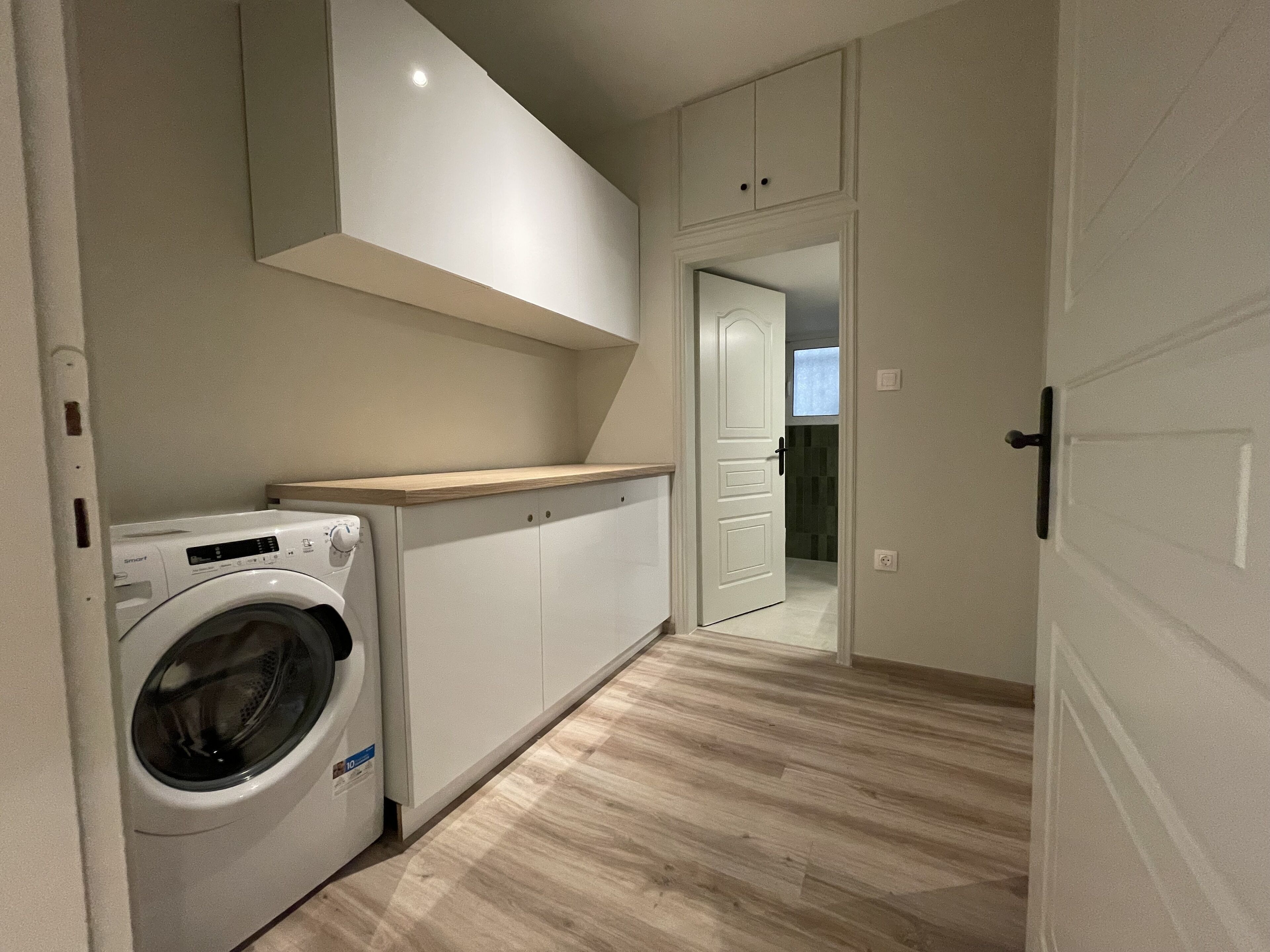 Une buanderie équipée d’un lave-linge, de placards et d’un plan de travail en bois.