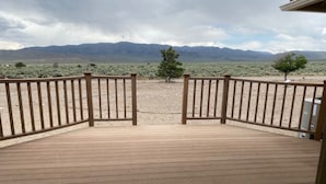 Una terraza de madera con barandilla de metal, que da a un paisaje desértico con vegetación escasa y montañas al fondo.