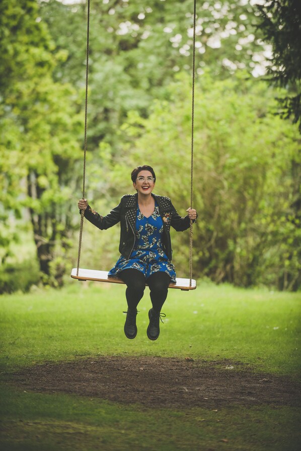 Una persona en un columpio en un parque, con follaje verde de fondo.