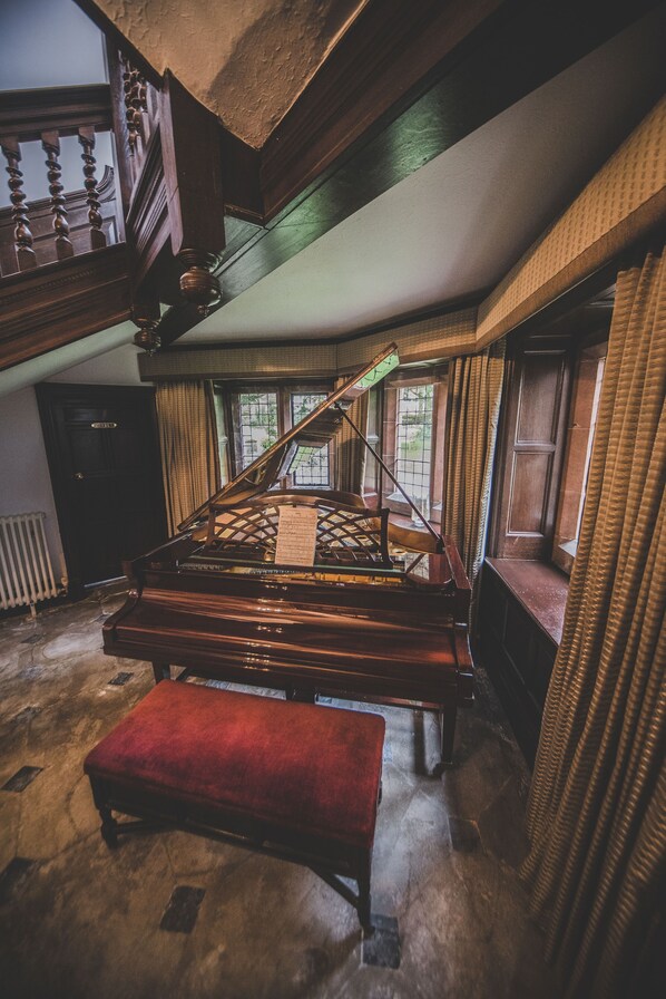 A grand piano in a spacious room with a high ceiling, large windows, and a red bench.