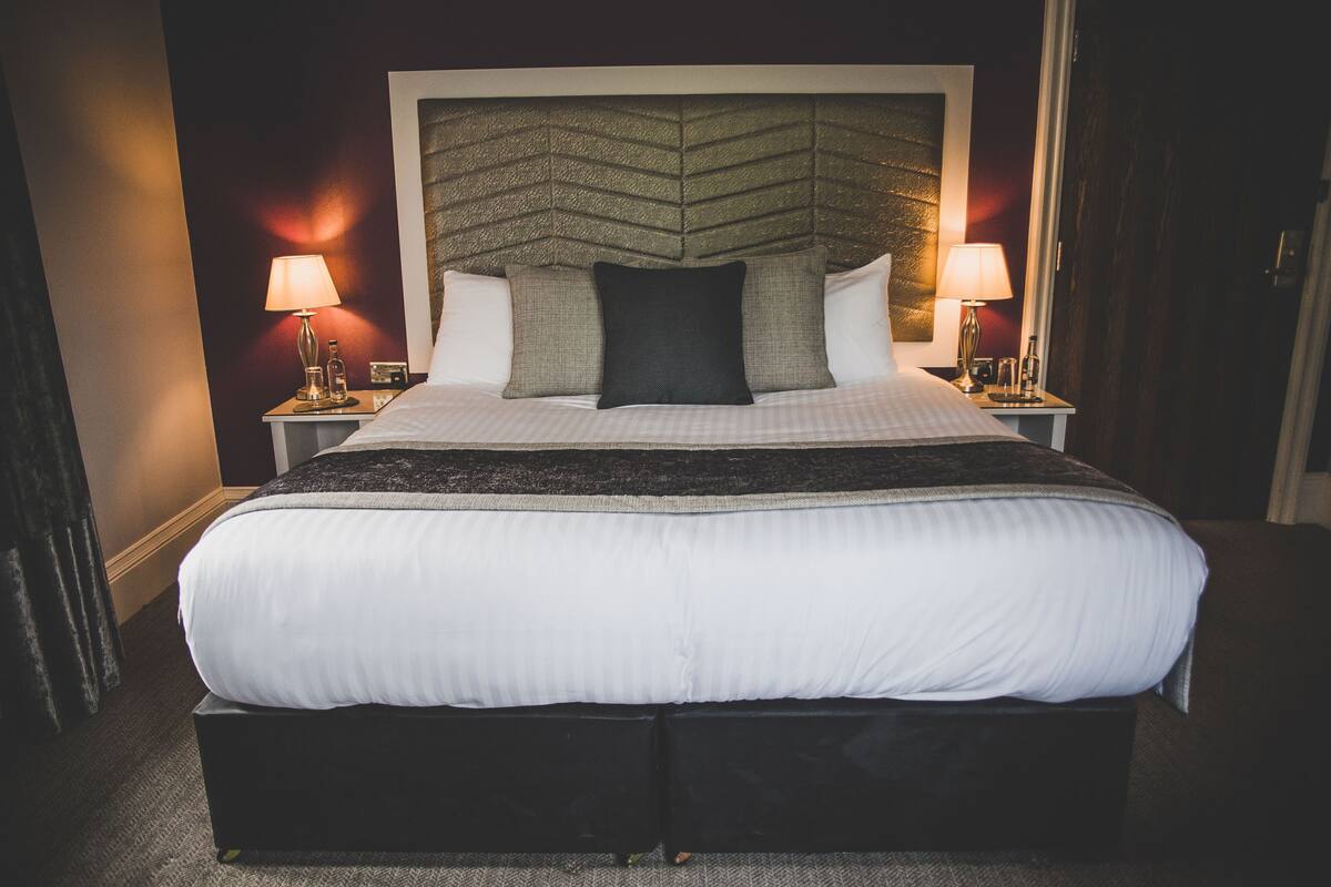 A large bed with a headboard, two bedside tables with lamps, and a dark-colored carpet.