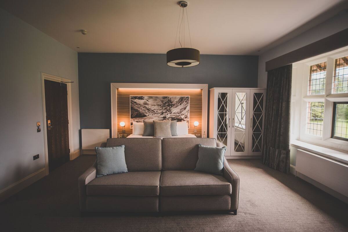 A modern living room with a sectional sofa, a large abstract painting, and a view of the outdoors through a window.