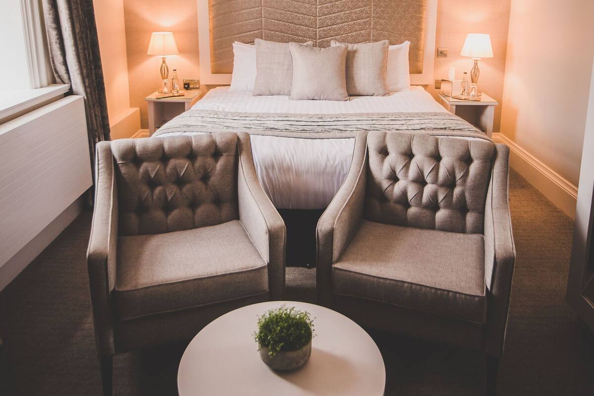 A hotel room with a large bed, two armchairs, a small table with a plant, and two bedside lamps.