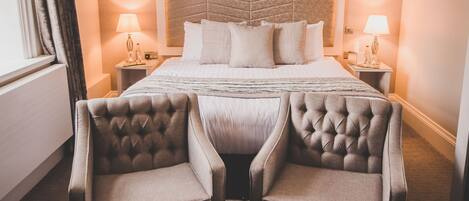 Een hotelkamer met een groot bed, twee fauteuils, een bijzettafeltje met een plant en twee bedlampen.
