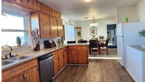 A kitchen with wooden cabinets, a dishwasher, and a dining area with a table and chairs. - Rustic retreat-near the Canyon (Canyon)
