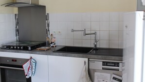 Una cocina con campana de acero inoxidable, un lavamanos negro sobre la encimera y un salpicadero de azulejos blancos.