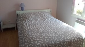 Un dormitorio con cama, mesita de noche, lámpara y ventana.