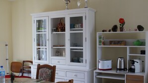 Un comedor con un armario blanco, sillas, una mesa con posavasos y diversos electrodomésticos de cocina.