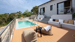 A modern villa with a swimming pool, outdoor seating, and a staircase leading to a balcony.