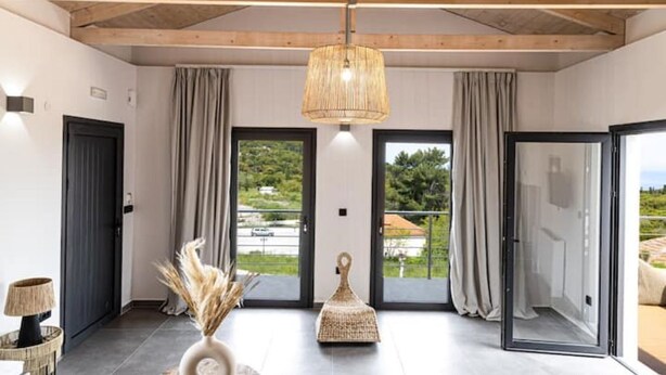 A spacious room with a high ceiling, large sliding glass doors leading to a balcony, and a hanging light fixture.