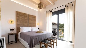 A bedroom with a bed, bedside tables, a small table, and a balcony with a view.