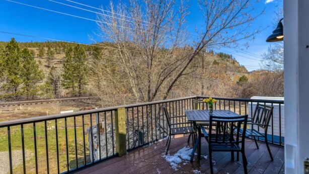 A wooden deck with a table and chairs, overlooking a train track and a hilly landscape. - Prickly Pear Studio Wolf Creek (Wolf Creek)
