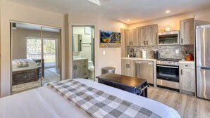 A modern kitchen with stainless steel appliances, a dining area with a wooden table, and a bedroom with a large bed and a balcony. - Prickly Pear Studio Wolf Creek (Wolf Creek)