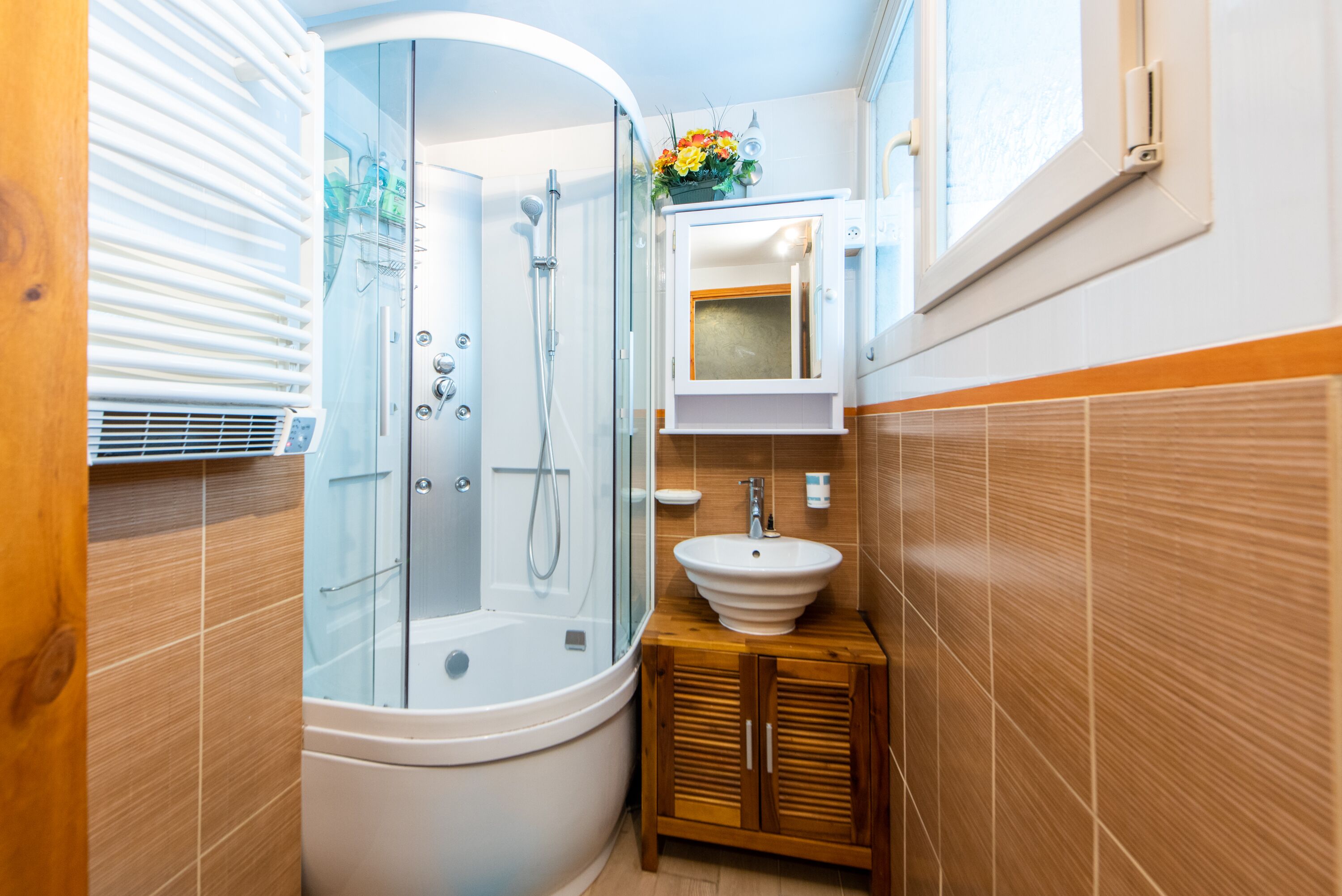 A modern bathroom with a glass-enclosed shower, a freestanding bathtub, a wooden vanity with a sink, and a mirror above the vanity.