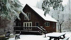 A wooden cabin with a porch, a picnic table, and benches.