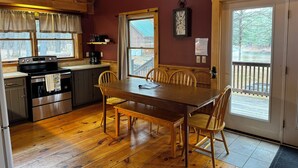 A cozy cabin kitchen with a wooden table, chairs, a stove, and a clock on the wall.
