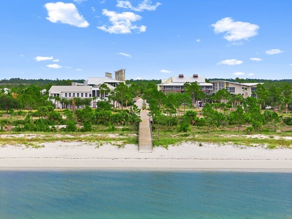A beachfront property with a large building, a wooden walkway, and a clear view of the ocean.