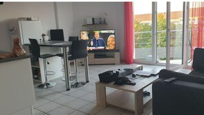 Un salon moderne comprenant un coin repas, un téléviseur et un balcon agrémenté de rideaux rouges.