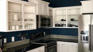 A modern kitchen with white cabinetry, a black countertop, stainless steel appliances, and a blue accent wall. - 5-star Luxury Apartment - Atop the Seagle Building (Gainesville)
