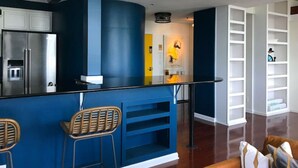 A modern kitchen with a blue accent wall, stainless steel appliances, and a bar area with two stools. - 5-star Luxury Apartment - Atop the Seagle Building (Gainesville)