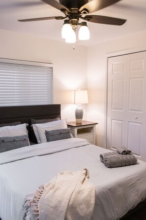 Une chambre à coucher avec un lit, un ventilateur de plafond, une lampe de chevet, une table de chevet et une porte.
