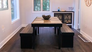 A spacious dining area with a wooden table and benches, a chandelier, and a view of the outdoors through large windows. - Updated Ann Arbor ranch w/private yard and lots of parking!  (Ann Arbor)
