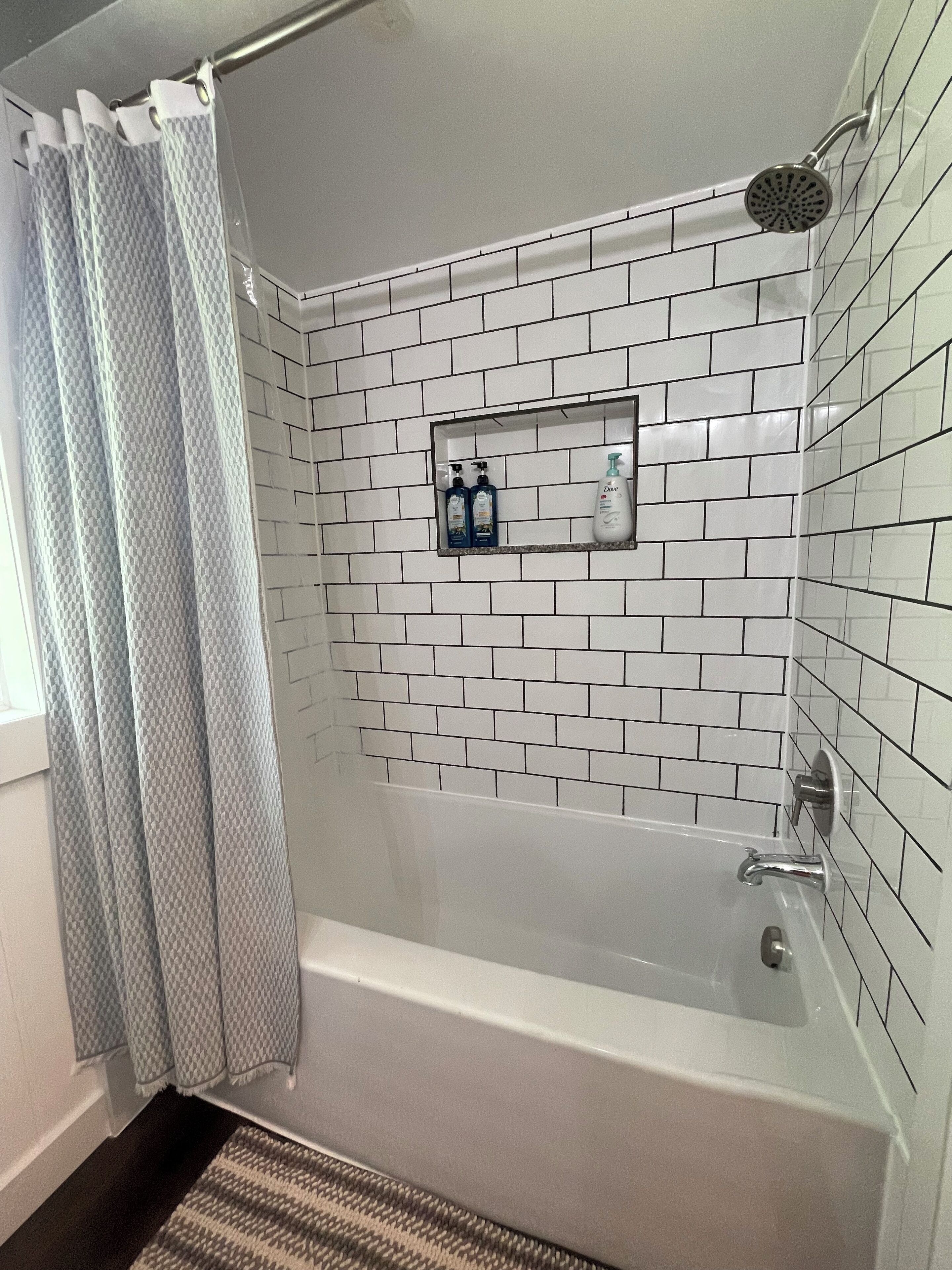 Une salle de bain avec une baignoire blanche, une pomme de douche et une étagère contenant des articles de toilette.