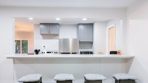A modern kitchen with a white countertop, stainless steel appliances, and three bar stools with cushioned seats. - Updated Ann Arbor ranch w/private yard and lots of parking!  (Ann Arbor)