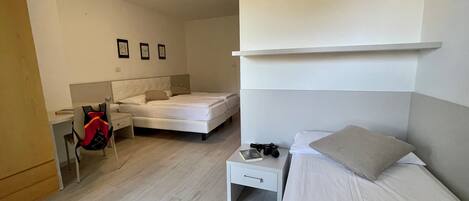 A hotel room with two beds, a desk, a chair, and a small table with a camera.