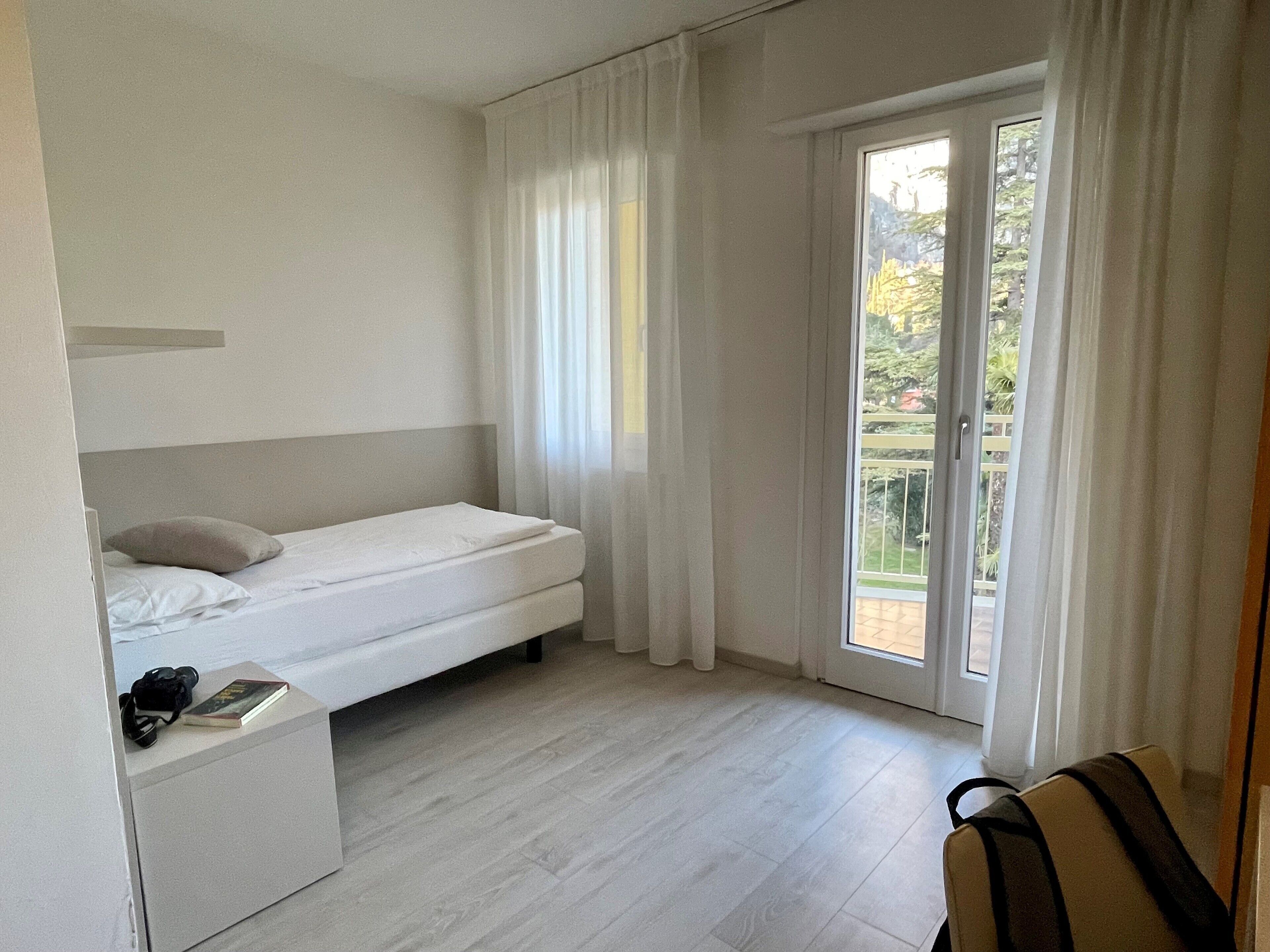 Et minimalistisk soveværelse med en enkeltseng, et lille natbord og udsigt til en balkon.