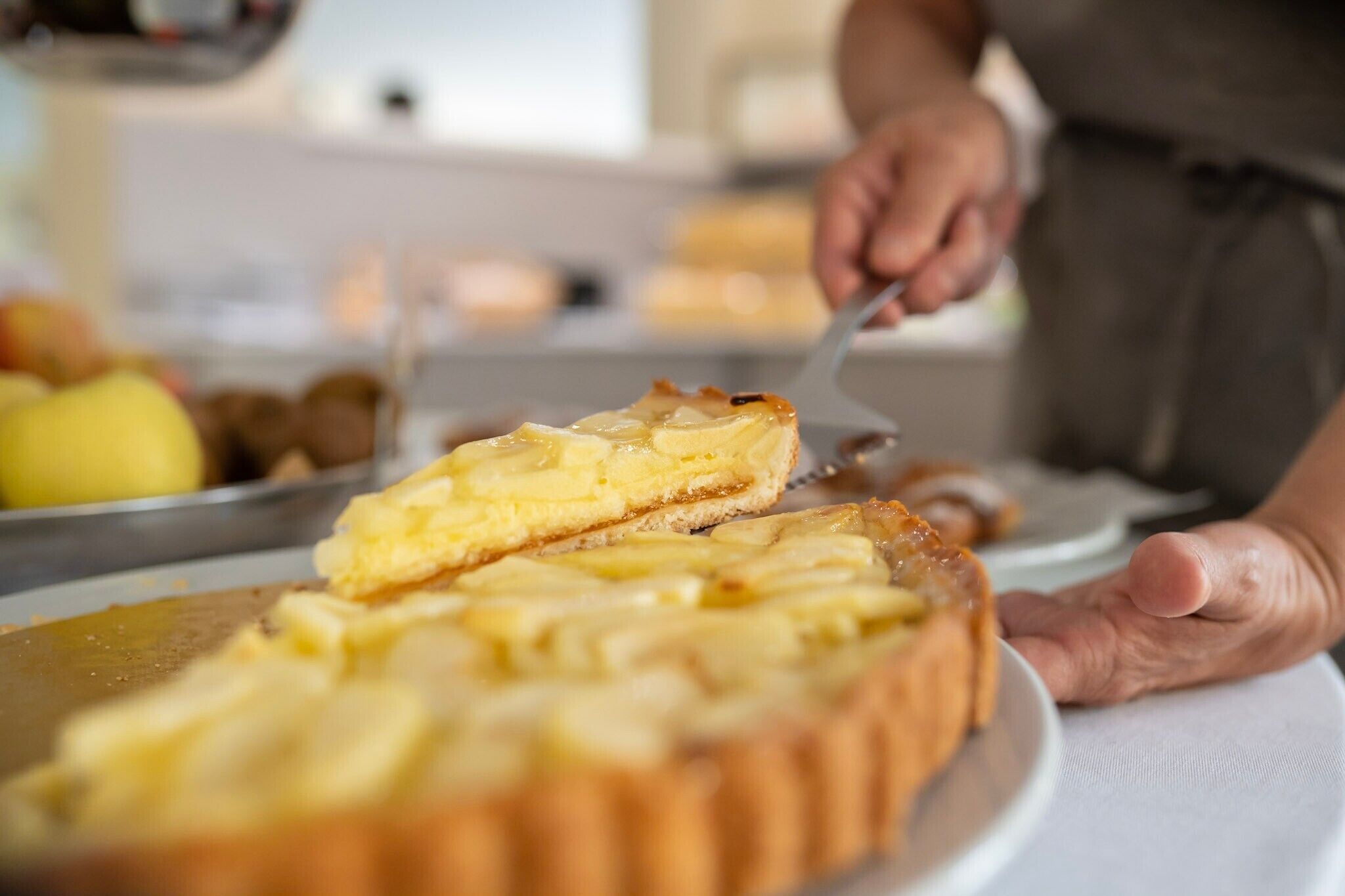 A person cutting a pie with a golden crust, likely apple pie, on a white plate.