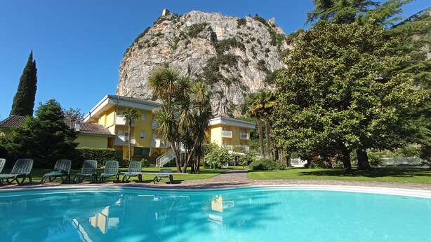 Un espace piscine offrant une vue dégagée sur une montagne en arrière-plan, un bâtiment jaune doté de balcons et plusieurs chaises longues.