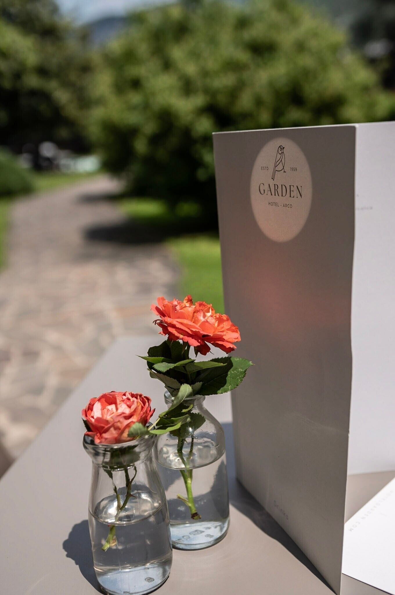 Two glass vases with flowers on a table next to a sign with the text "GARDEN HOTEL - ARCO".