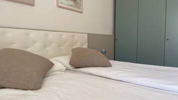 A neatly made bed with white linens and two beige pillows, a tufted headboard, and a light green wardrobe in the background.