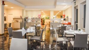 Un vaste espace dédié à la salle à manger, avec plusieurs tables et chaises, une cuisine à l’arrière-plan et un sol en marbre poli.