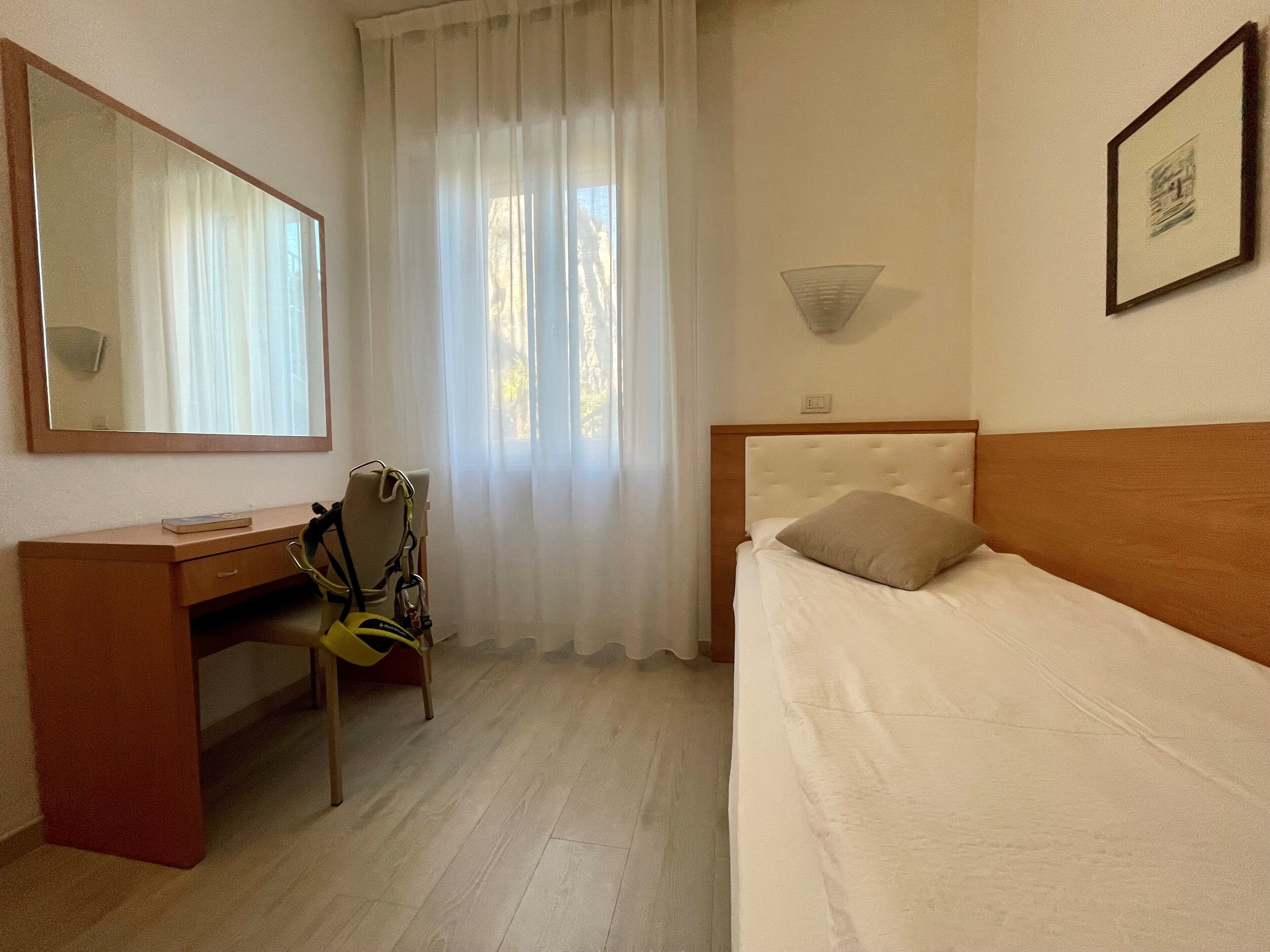 A hotel room with a bed, a desk, a chair, a mirror, and a window with curtains.