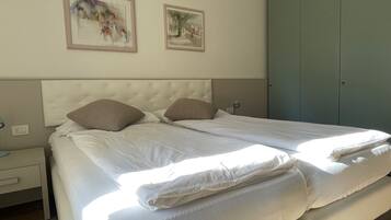 Una cama doble con ropa blanca, un cabecero capitonado y dos cuadros enmarcados en la pared.