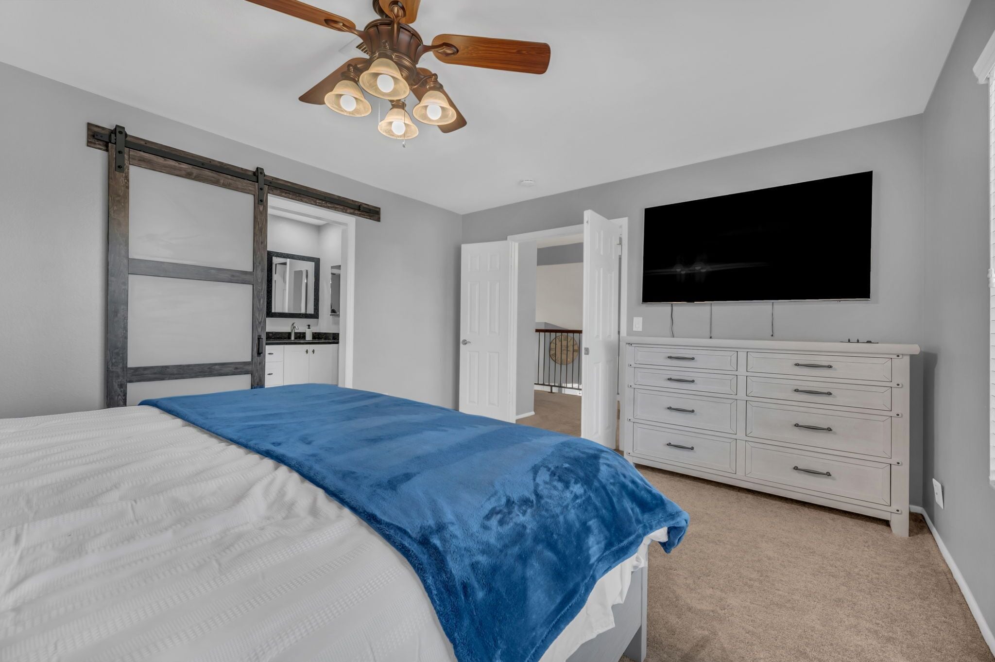 A bedroom with a bed, a dresser, a ceiling fan, and a TV.