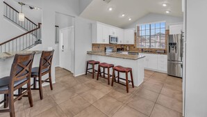 Una cocina amplia con una isla grande, armarios blancos y un refrigerador de acero inoxidable.