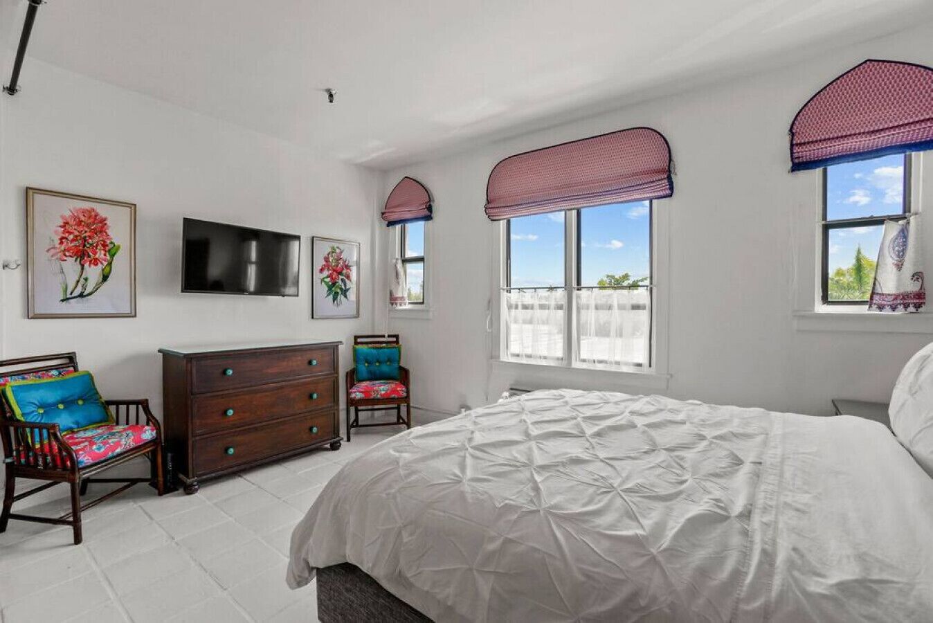 Une chambre avec un grand lit, une commode, deux chaises, un téléviseur et une fenêtre donnant sur l’extérieur.