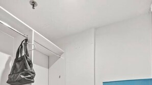 A compact room with a wardrobe, a blue refrigerator, and a storage unit with drawers.