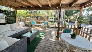 A covered outdoor patio with wicker furniture, a white table, and a green artificial turf floor.