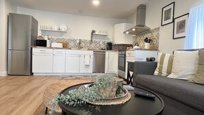 A modern kitchen with white cabinets, a stainless steel refrigerator, and a microwave. There is a dining area with a gray sofa and a round black coffee table.
