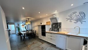 Une cuisine moderne avec des meubles blancs, un coin repas comprenant une table et des chaises, et une œuvre d’art représentant un crabe, accrochée au mur.