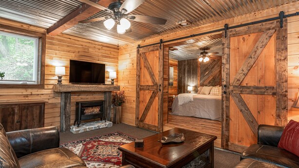 Interior rústico de una cabaña con chimenea, muebles de cuero y paredes de madera.