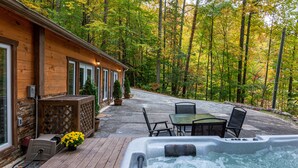 Una cabaña de madera con jacuzzi, mobiliario de patio y vistas a un bosque.